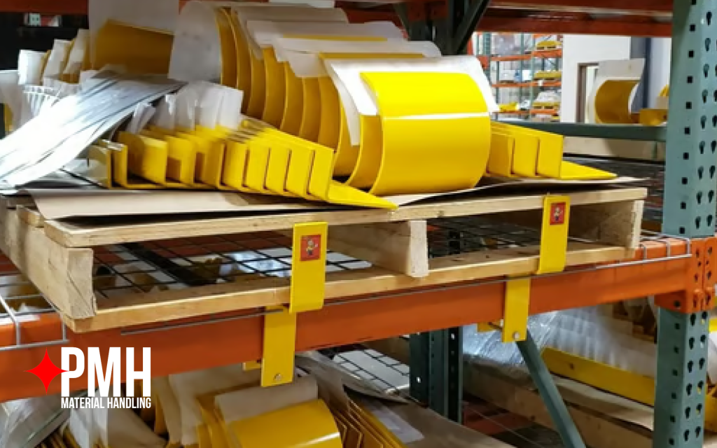 Yellow pallet rack safety clips and column guards stored on a wooden pallet inside a warehouse — PMH Material Handling