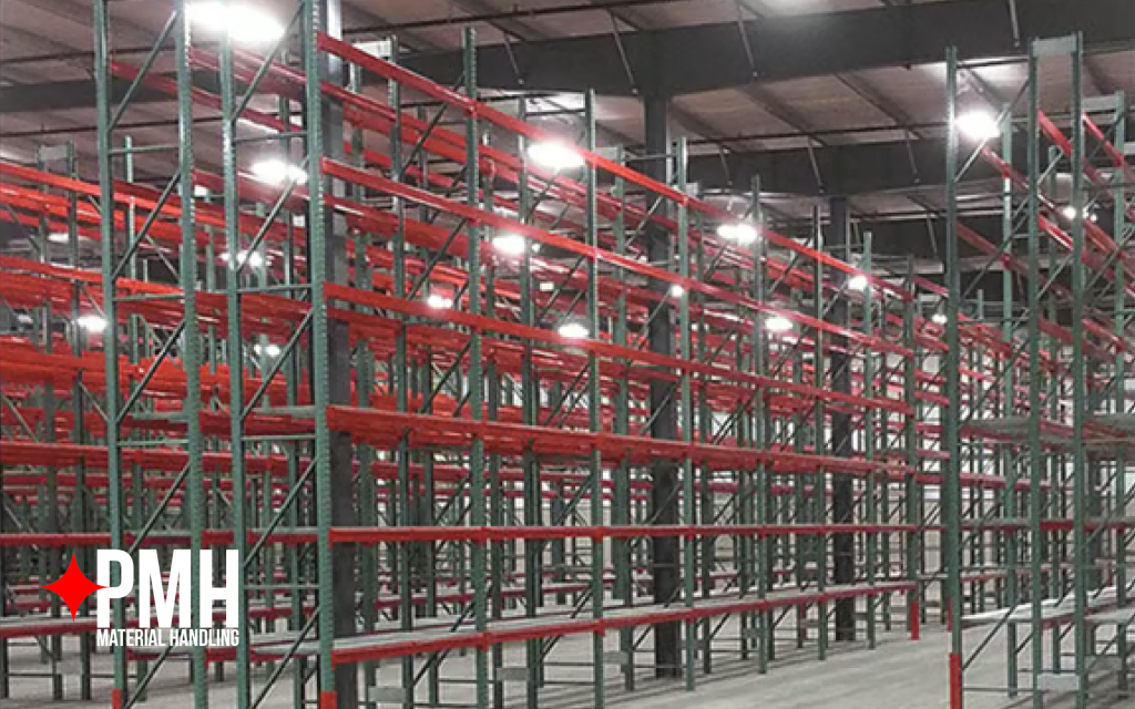 Large warehouse interior featuring multiple rows of tall green and red pallet racking systems with bright overhead lighting — PMH Material Handling
